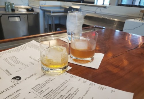 Three glasses of cocktails on a wooden bar top, with a drink menu partially visible.