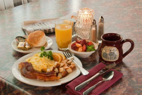 A breakfast spread featuring an omelet, potatoes, fruit, orange juice, a biscuit, and a coffee mug on a table.