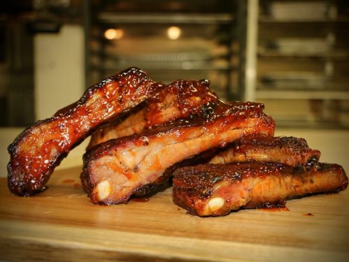 A stack of glazed barbecue ribs on a wooden cutting board, showcasing a rich, sticky sauce and smoky texture.