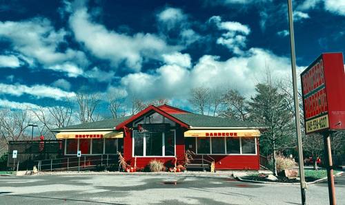 A red barbecue restaurant with yellow awnings, surrounded by autumn decorations and a cloudy blue sky.