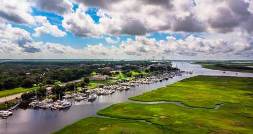 Aerial view of a marina with boats, lush green grass, and a cloudy sky over a calm waterway.