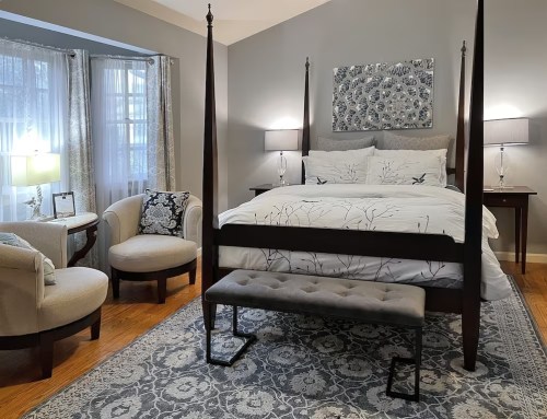 Cozy bedroom featuring a four-poster bed, armchairs, and soft lighting, with elegant decor and a patterned rug.