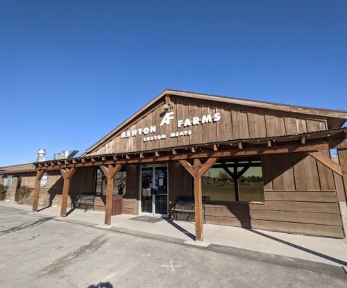 Exterior of Ashton Farms, a rustic wooden building with a sign for custom meats, under a clear blue sky.