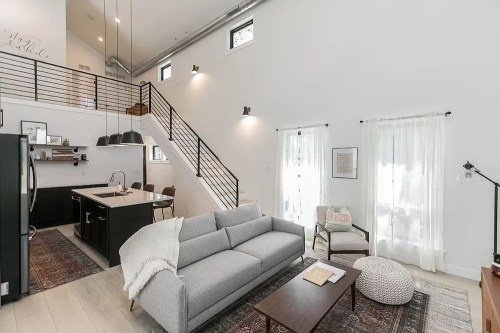Modern living room with a gray sofa, wooden coffee table, and a staircase leading to a loft area, bright and airy design.
