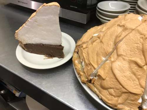 A slice of meringue-topped pie on a plate next to a whole pie with a fluffy, golden meringue layer.