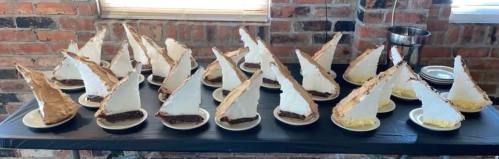 A table with multiple plates of dessert, featuring slices of pie with meringue topping arranged in a row.