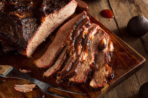 Sliced smoked brisket on a wooden cutting board, with a knife and sauce nearby.