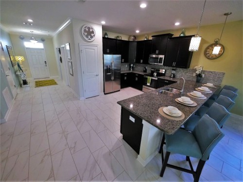 Modern kitchen with dark cabinets, granite countertops, stainless steel appliances, and a breakfast bar with four stools.