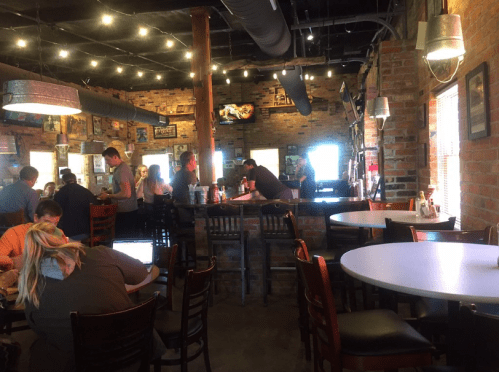 A cozy restaurant interior with brick walls, wooden tables, and patrons enjoying their meals and drinks under warm lighting.