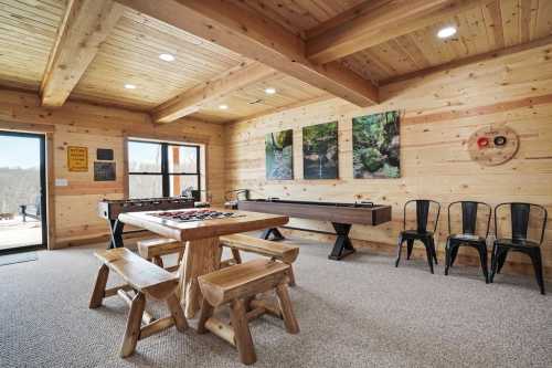 Cozy wooden game room with a table, chairs, and artwork on the walls, featuring large windows and a rustic vibe.