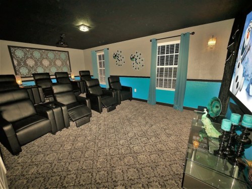 Home theater room with black reclining chairs, blue accents, and a large screen, featuring decorative wall elements.