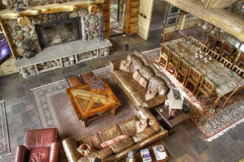 A spacious rustic living room with a stone fireplace, leather sofas, a wooden coffee table, and a dining area.