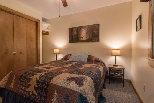 Cozy bedroom with a quilted bedspread, two lamps, and a nature-themed wall art featuring a deer in a forest.
