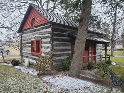 A rustic log cabin with red accents, surrounded by snow and trees in a peaceful outdoor setting.