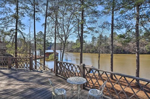 A serene lakeside view from a wooden deck, featuring trees and a small table with chairs overlooking the water.