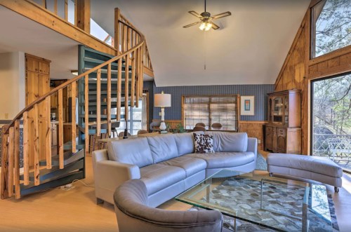 Cozy living room with a spiral staircase, large windows, and wooden accents, featuring a sectional sofa and glass coffee table.