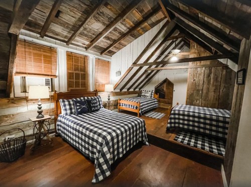 Cozy attic bedroom with wooden beams, plaid bedding, and two beds, featuring warm lighting and rustic decor.