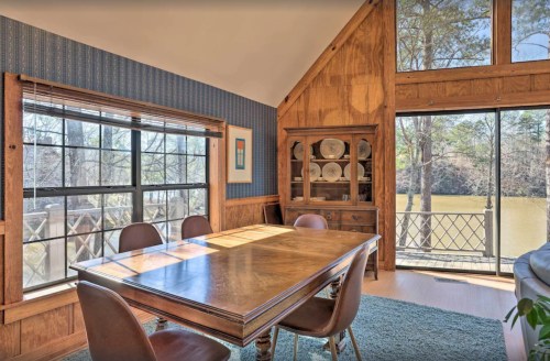 Cozy dining area with a wooden table, chairs, and large windows overlooking a serene outdoor view.