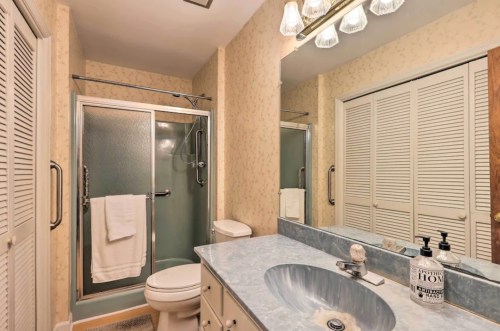 A bathroom featuring a shower, toilet, sink with blue countertop, and light-colored wallpaper.