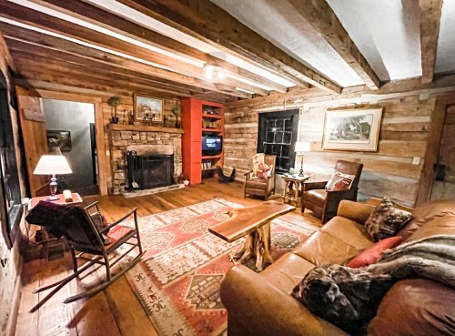 Cozy rustic living room with wooden beams, stone fireplace, comfortable seating, and warm lighting.