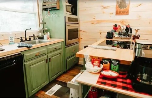 Cozy kitchen with green cabinets, wooden accents, modern appliances, and a coffee station on a checkered cloth.
