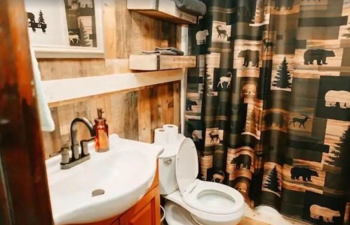 Cozy bathroom featuring a wooden decor, a toilet, sink, and a patterned shower curtain with wildlife motifs.