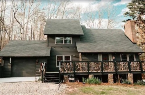 A dark wooden house with a sloped roof, surrounded by trees, featuring a front porch and a garage.