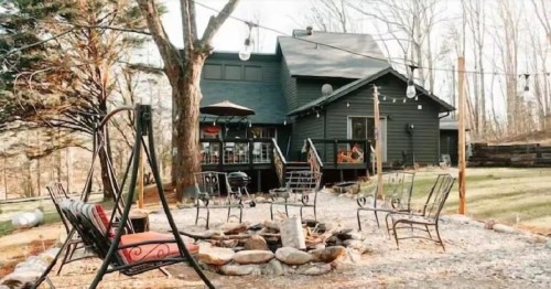 A cozy outdoor space with a fire pit, seating, and a dark house surrounded by trees in a serene setting.