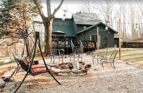 A cozy outdoor space with a fire pit, chairs, and a house surrounded by trees, creating a serene atmosphere.