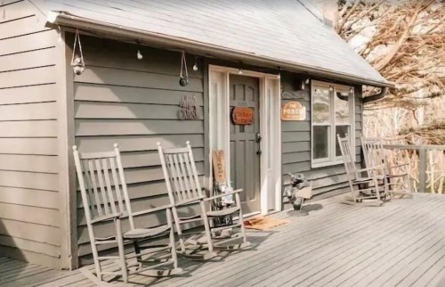 A cozy gray house with a welcoming front door and two rocking chairs on a wooden deck.