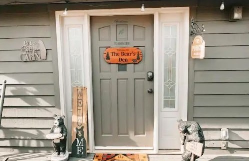 A cozy entrance with a gray door, bear-themed decor, and a welcome mat reading "The Bear's Den."