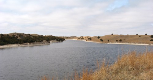 Wide shot of Calamus Reservoir in Nebraska showing blue water and rolling tan sandhills.