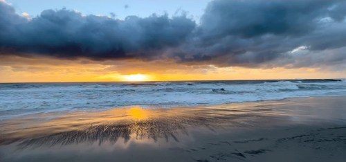 A serene beach at sunset, with waves gently lapping the shore and dramatic clouds in the sky.