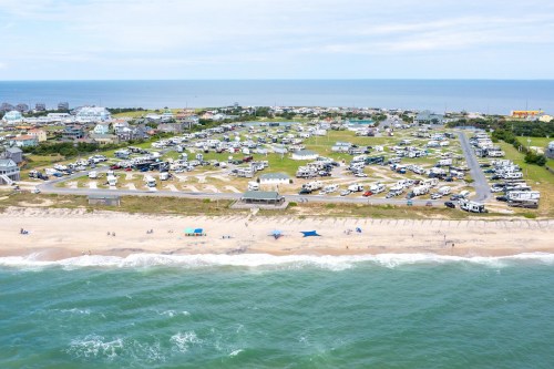 Aerial view of a beachside RV park with campers, green spaces, and the ocean in the background.