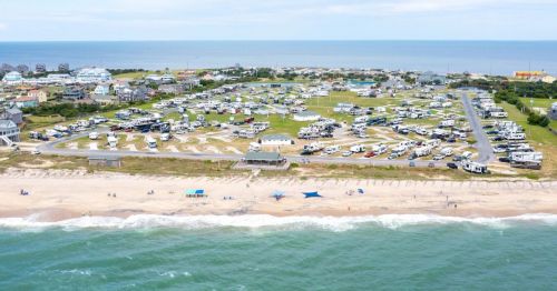 Aerial view of a beachside RV park with numerous campers, sandy beach, and ocean waves in the background.