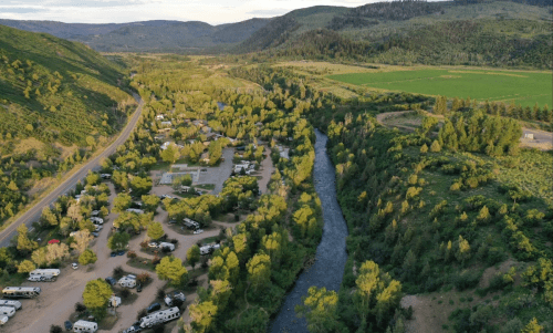 Aerial view of a lush green valley with a winding river, surrounded by campsites and mountains in the background.
