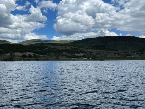 A serene lake surrounded by green hills and a partly cloudy sky, reflecting the landscape on the water's surface.