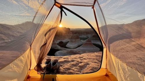 View from a tent at sunrise, showcasing colorful rock formations and a serene landscape.