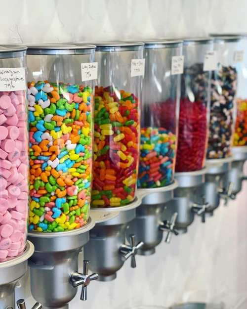 A row of clear dispensers filled with colorful candies, including gummies, chocolates, and pastel sweets.