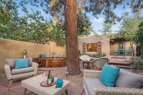 Cozy outdoor seating area with a hot tub, surrounded by trees and a charming adobe-style home in the background.