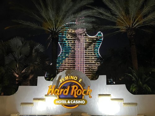 Illuminated Hard Rock Hotel & Casino sign with a guitar-shaped building and palm trees at night.