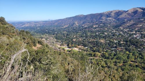 A panoramic view of a lush valley surrounded by mountains under a clear blue sky.