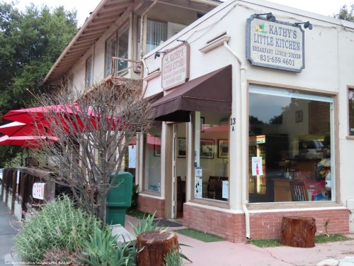 A cozy restaurant exterior with a sign reading "Kathy's Little Kitchen," featuring outdoor seating and greenery.