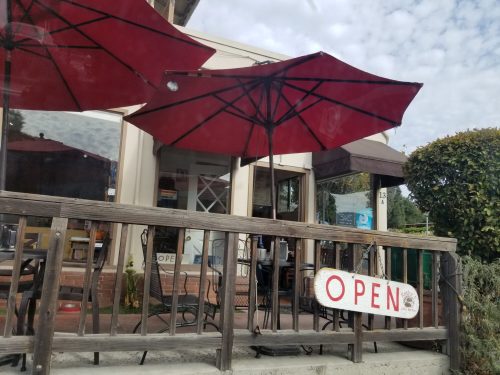 A café with red umbrellas outside, featuring an "OPEN" sign on a wooden railing.