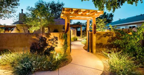 A beautifully lit pathway leads through a garden with a wooden pergola and lush greenery at dusk.