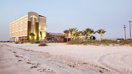 A beachfront hotel at dusk, surrounded by palm trees and sandy beach, with soft lighting illuminating the exterior.