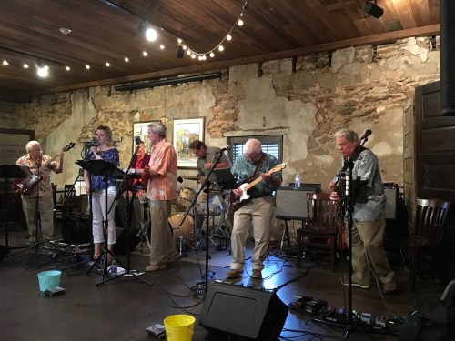 A live band performs on stage in a rustic venue with exposed brick walls and wooden beams.