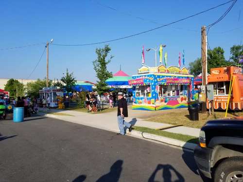 A vibrant outdoor fair scene with colorful booths, people enjoying the festivities, and clear blue skies.