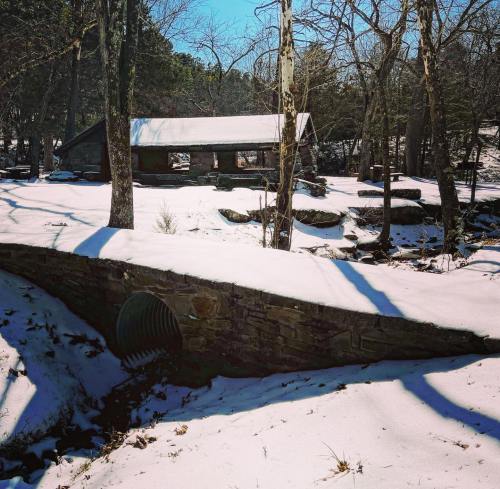 A snowy landscape featuring a stone bridge, a small building in the background, and bare trees under a clear blue sky.