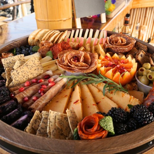 A beautifully arranged charcuterie board with cheeses, meats, fruits, nuts, and garnishes on a wooden platter.